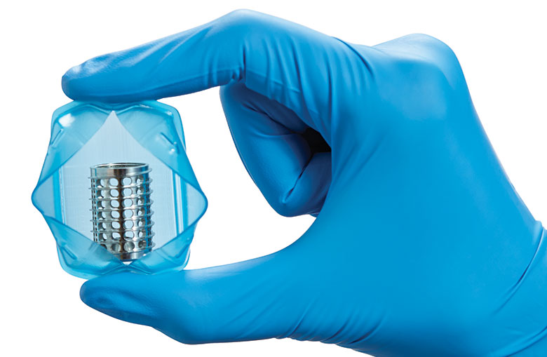 Blue-gloved hand holding a transparent container with a metal cylinder filled with white pellets