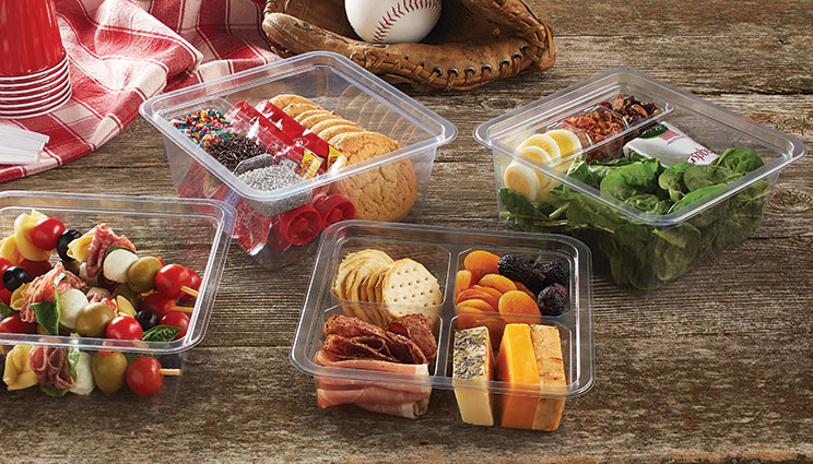 Four containers filled with picnic foods, including skewers, sandwiches, salad, and assorted cheese, meat, fruit, and crackers