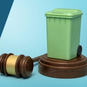 Green wheelie bin on a wooden platform beside a judge’s gavel
