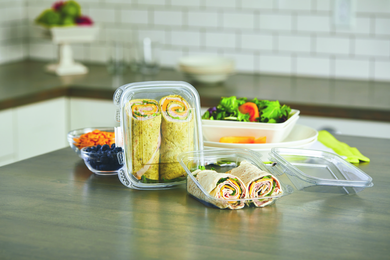 Clear containers hold sliced tortilla wraps, salad, carrots, and blueberries on a kitchen counter