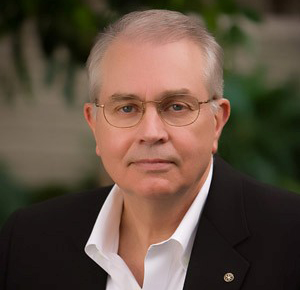 Man with gray hair and glasses wearing a black suit jacket and white shirt