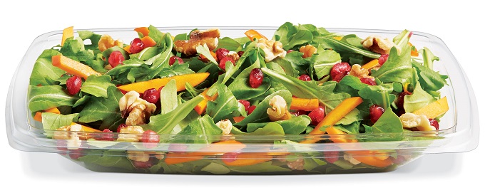 Mixed green salad with carrots, pomegranate seeds, walnuts, and tomatoes in a clear container