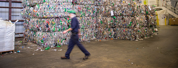 Worker walking past bales of compacted plastic recyclables in a recycling facility