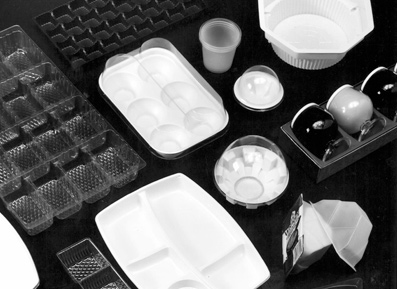 Various disposable plastic food containers, trays, cups, and packaging arranged on a dark surface