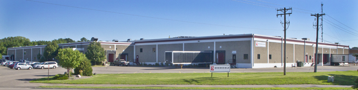 Long industrial building with a parking lot, trees, utility poles, and a Brookdale sign