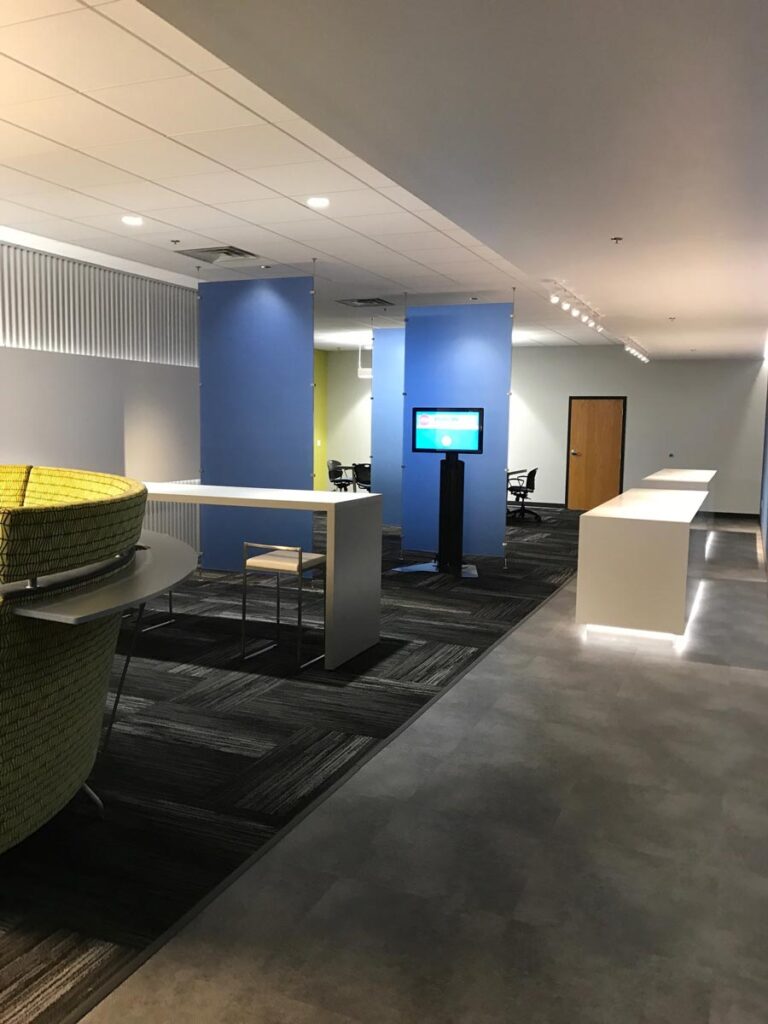 Modern office lobby with blue partition walls, a digital display, white counters, and lounge seating