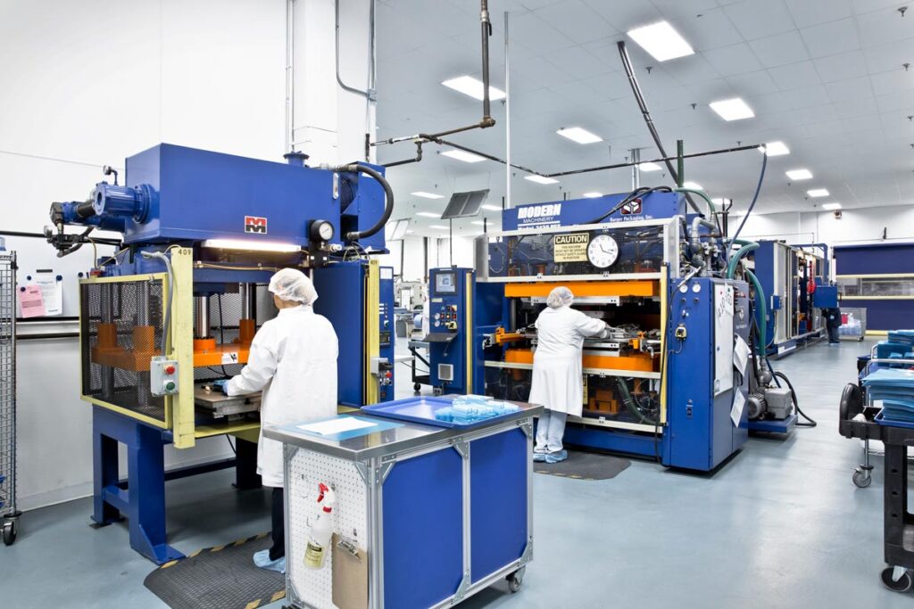 Two workers in protective clothing operate industrial presses in a clean manufacturing facility