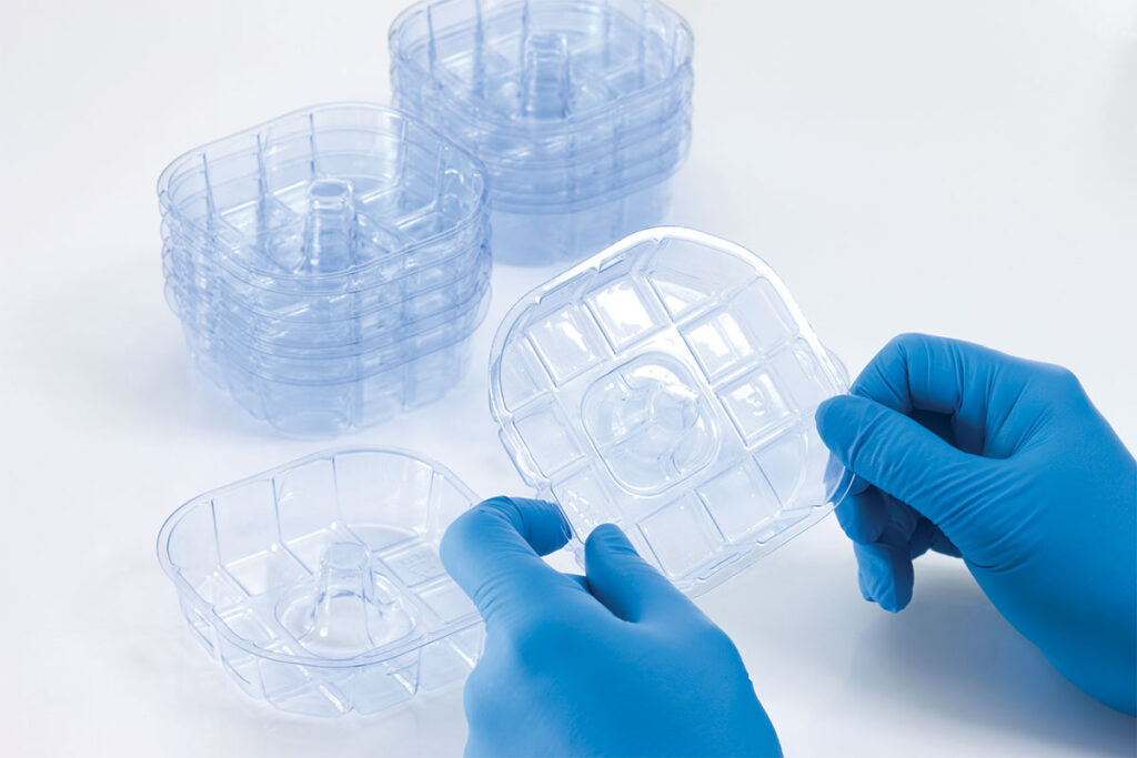 Gloved hands inspect a clear plastic tray among stacked trays